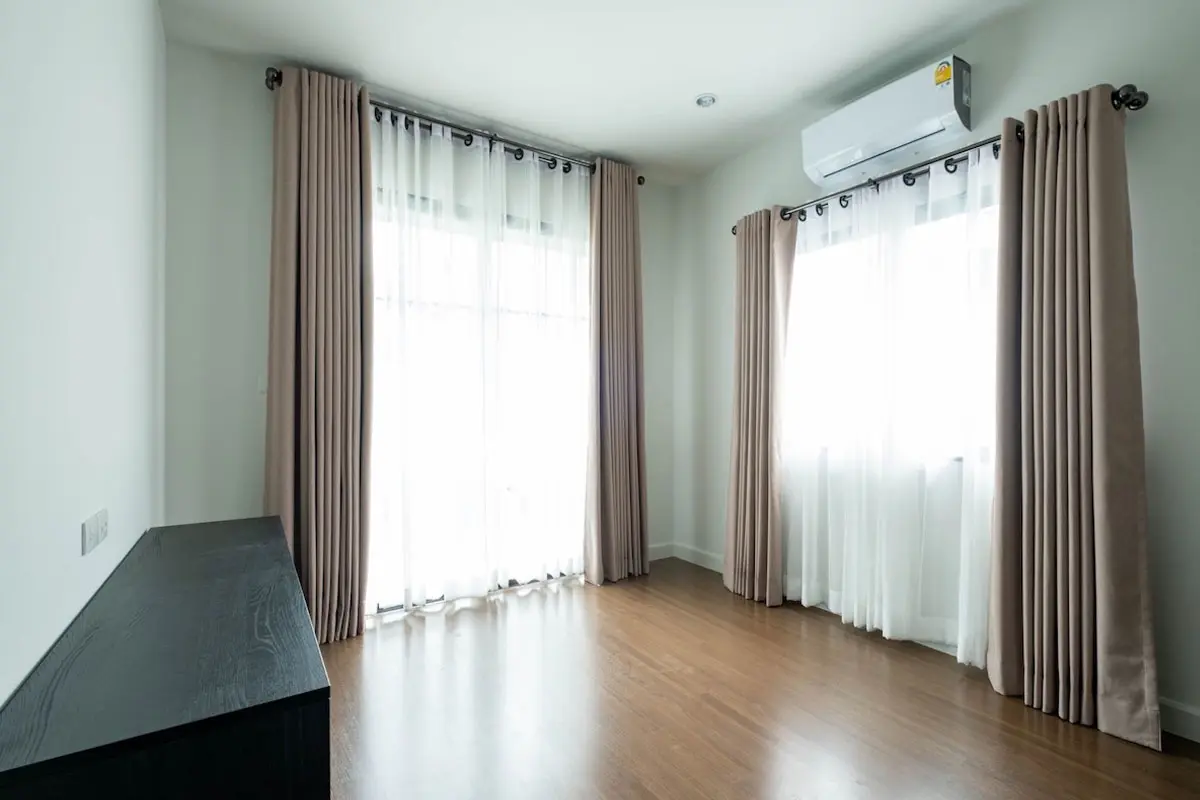 Minimalist room with beige eyelet-style curtains, sheer white layers, and wooden flooring, creating a simple and airy space.