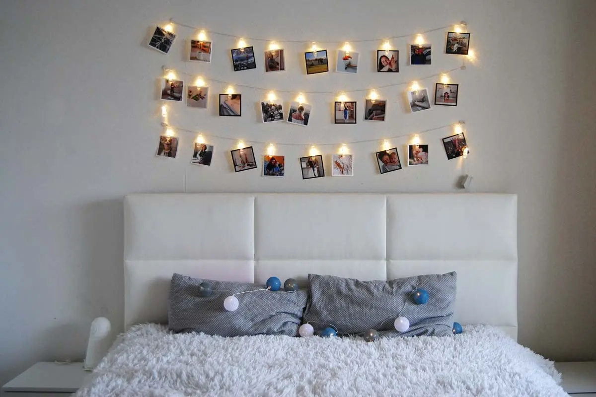 Bedroom with a display of family photos hung on string lights above a white headboard, creating a warm and personal touch.