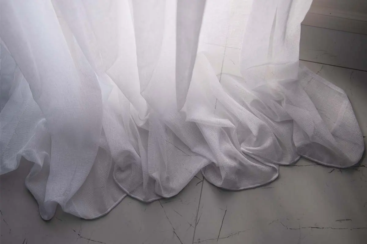 Sheer white curtains gently pooling on the floor with soft folds.