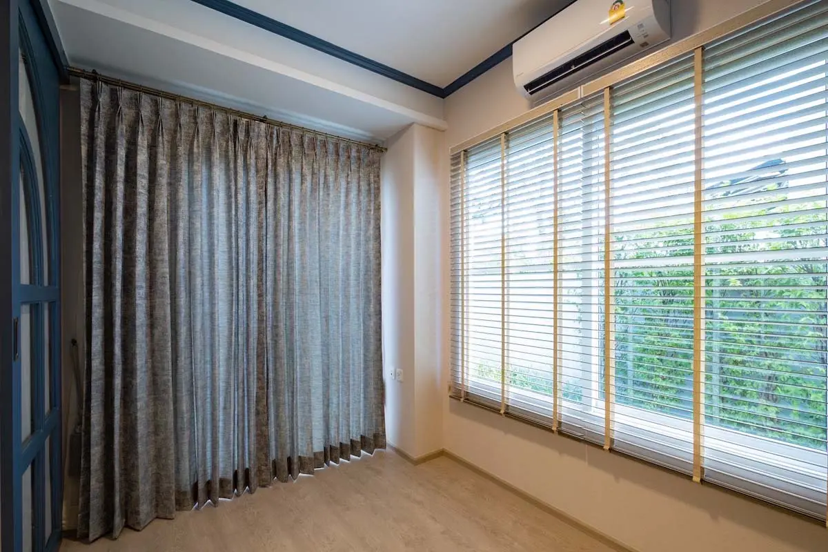 Room with triple pinch pleat curtains and wooden blinds on large windows.