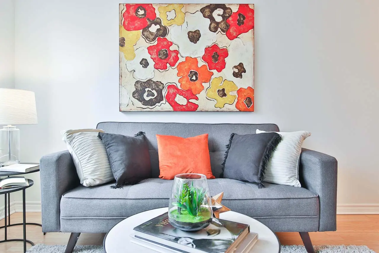 Living room with a gray sofa and a wall painting decorated with vibrant red, yellow, and black flowers.