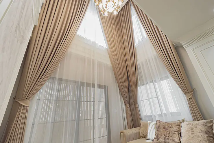 Room with a double-height ceiling, both sheer and blackout curtains elegantly drape the tall, large windows.