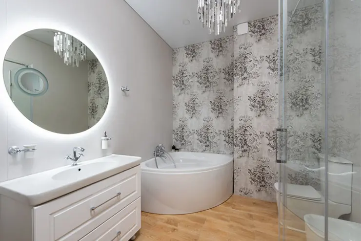 Modern bathroom with ornate wallpaper and a round mirror.