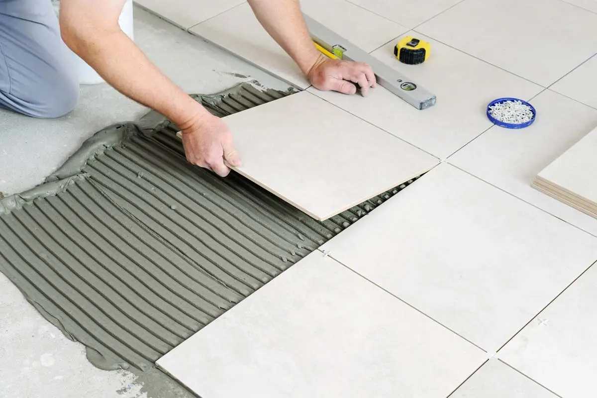 Man installing ceramic floor tiles, aligning them carefully with adhesive.