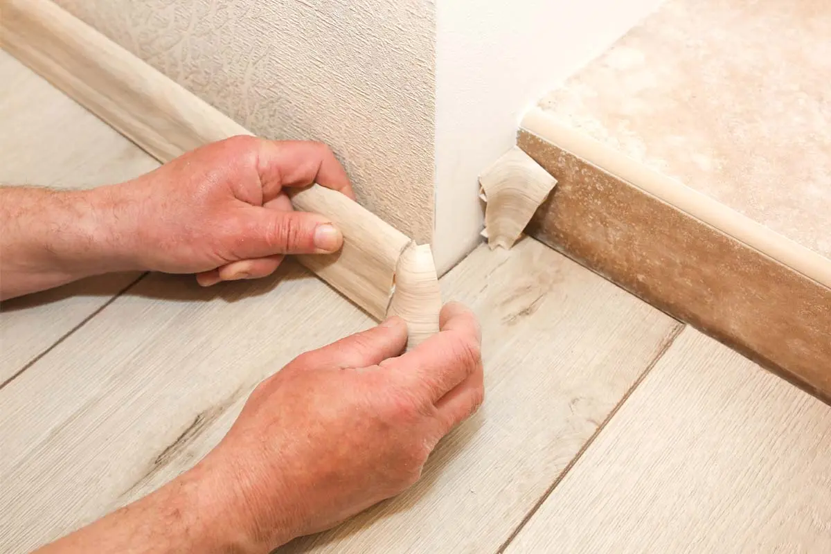 Hands are installing skirting boards along a corner wall and staircase.