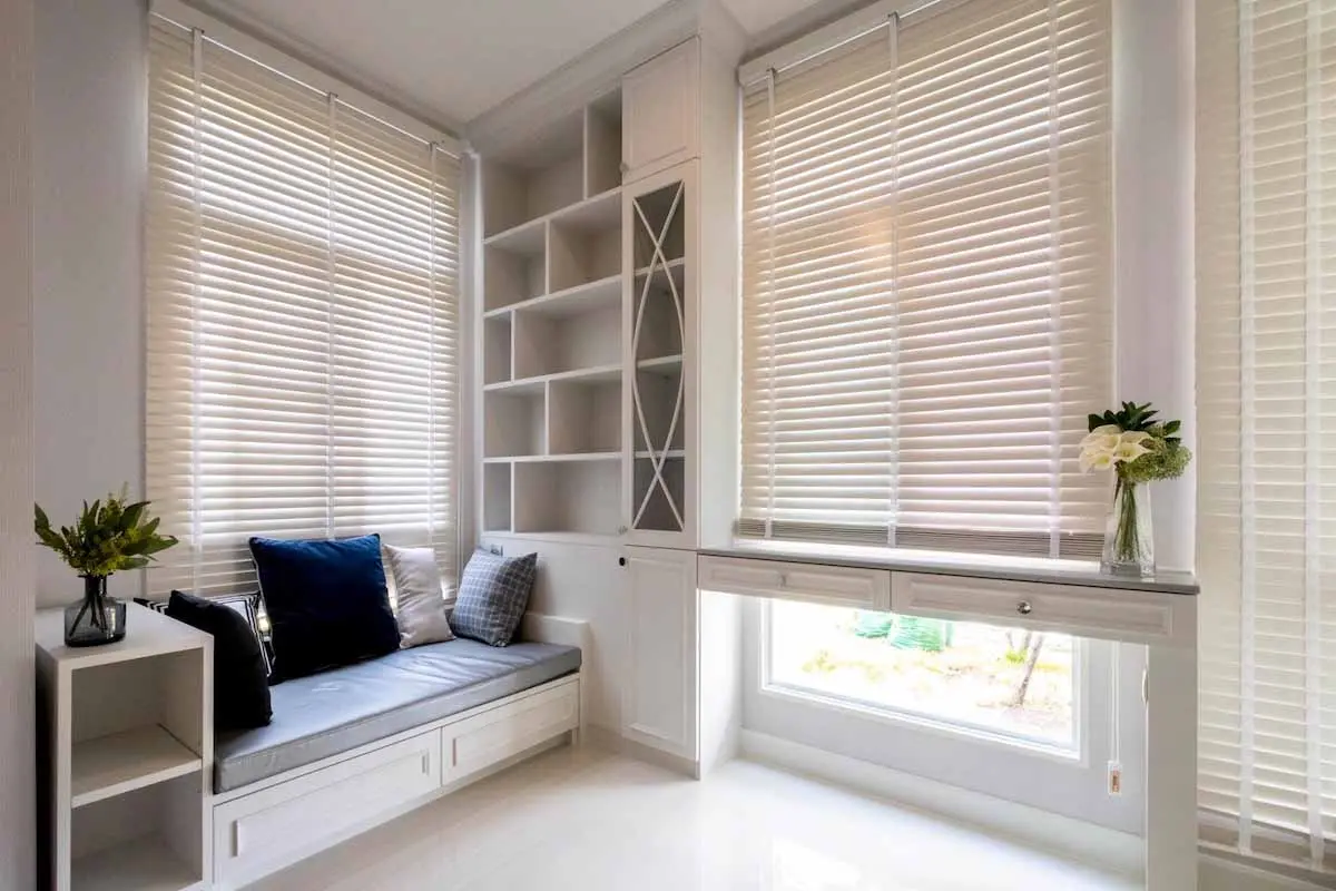 Cozy nook with white basswood blinds, built-in shelves, and a cushioned bench with decorative pillows.