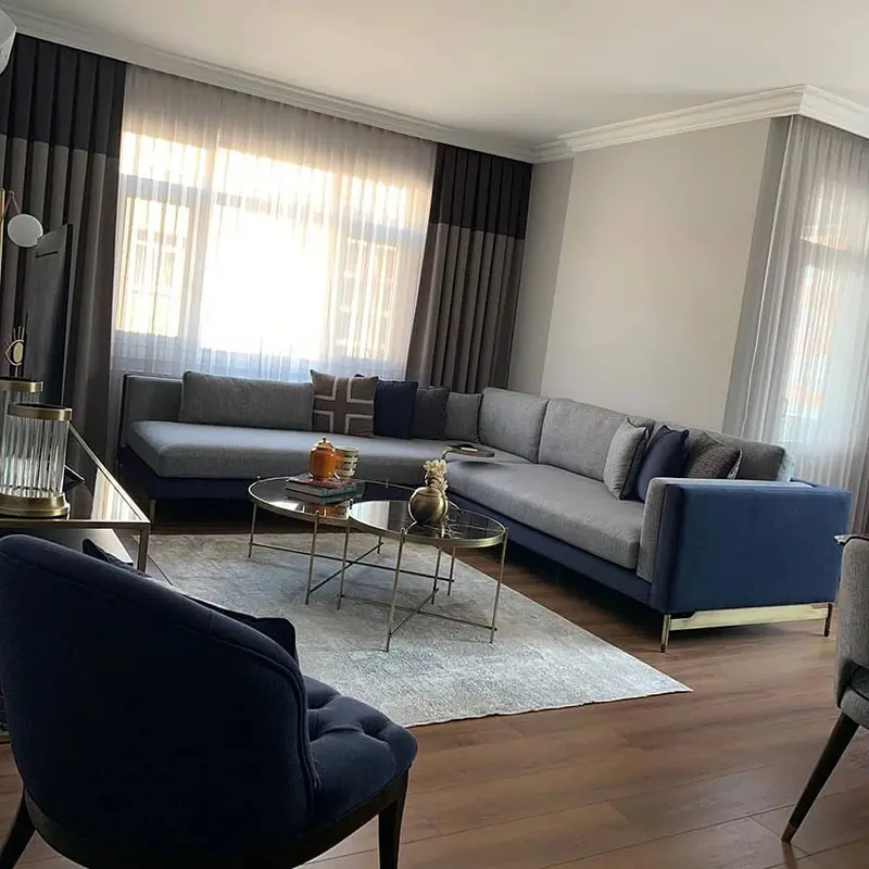 Living room with gray area rug, gray sectional sofa, glass coffee table and dual gray curtains.