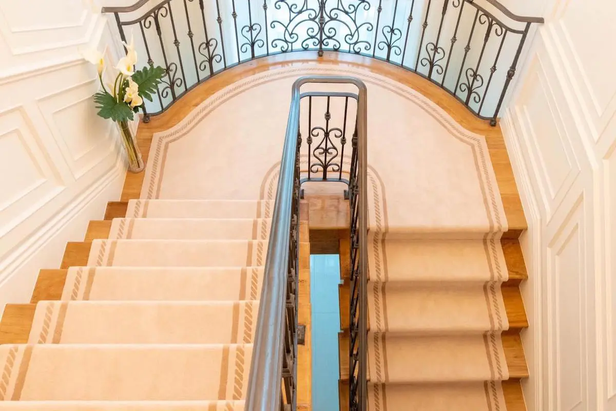 Staircase with beige carpet and black iron railings, viewed from above.