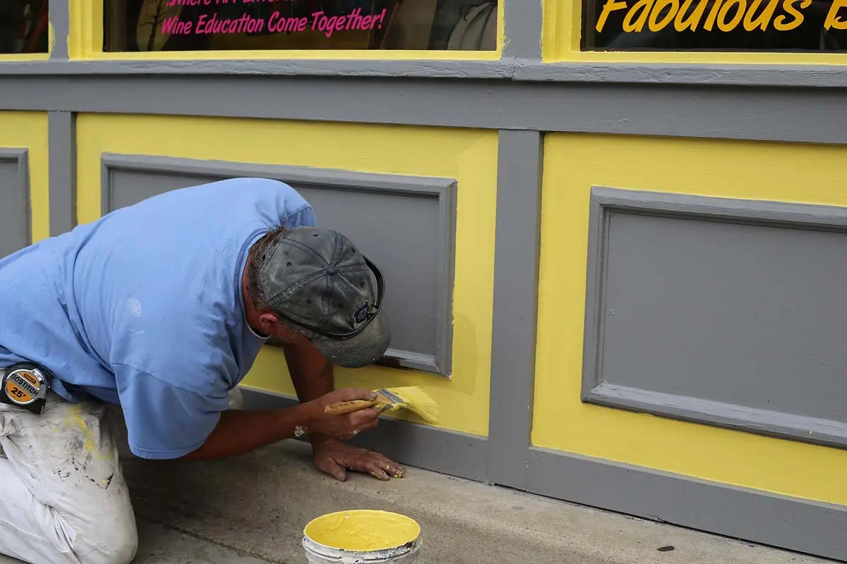 Man painting yellow trim on a storefront.