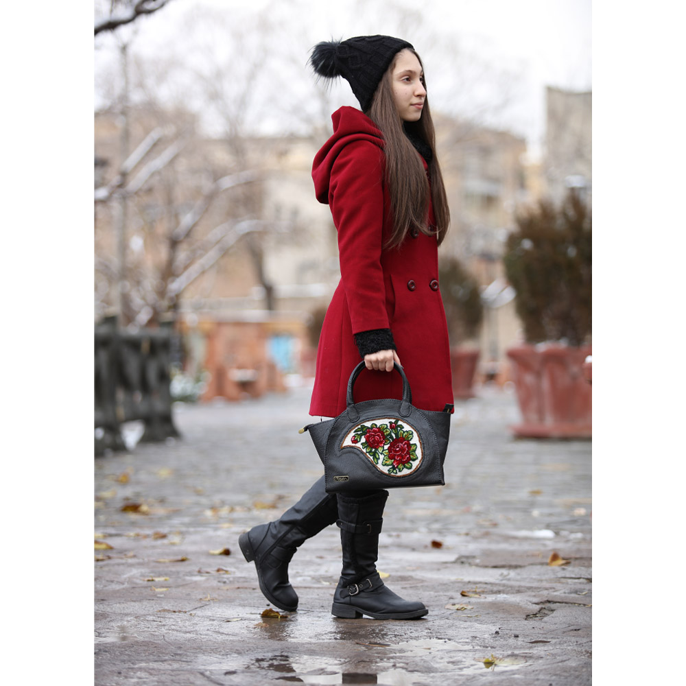 Woman in red coat holding black embroidered bag.