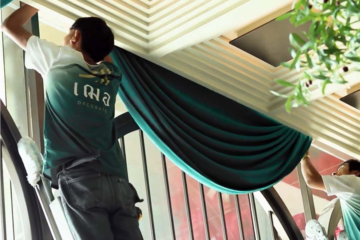 Cher Decor team installing green colored velvet curtains on tall window.