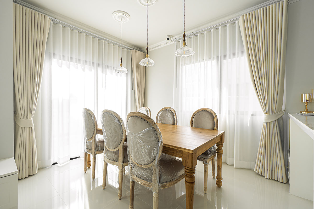 Dining area with cream dimout curtains, wooden table, and upholstered chairs.