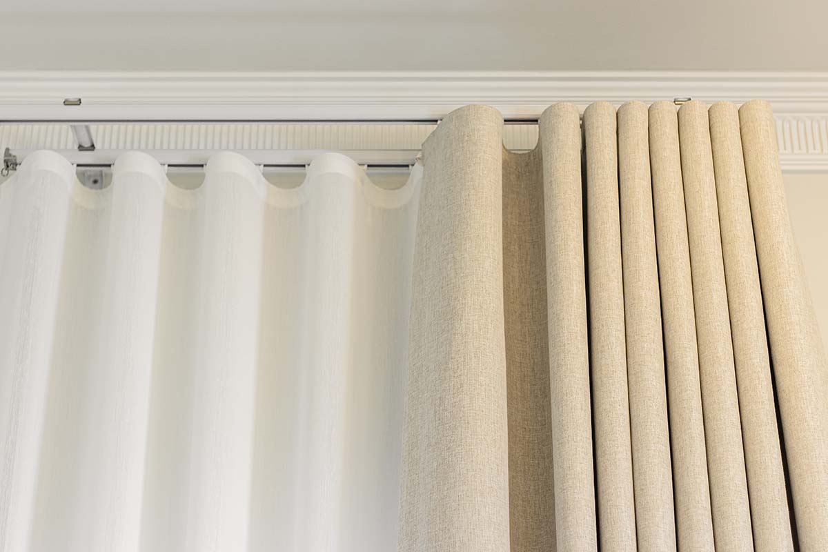 Close-up of sheer and dimout cream curtains on a curtain rod.