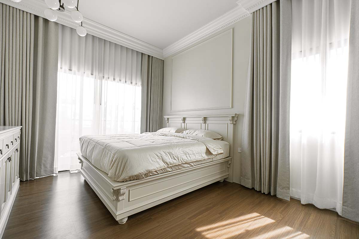 Elegant bedroom with gray blackout and white sheer curtains and a white bed.