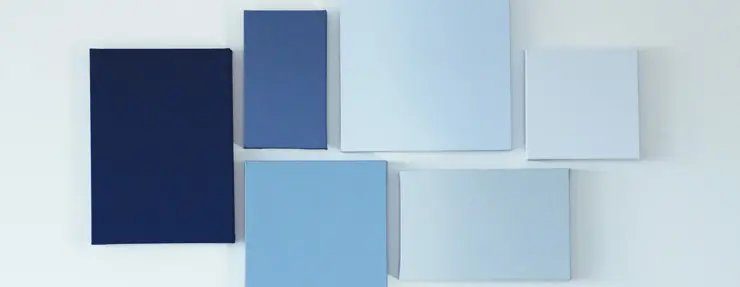 Various shades of blue canvas squares arranged on a white wall.