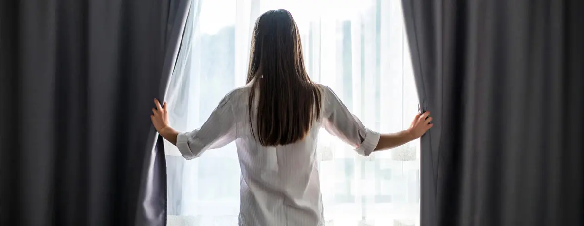 A woman is pulling apart a set of curtains that consist of two layers