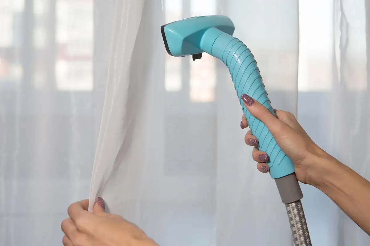 A woman using a curtain steamer to clean and iron a sheer curtain.