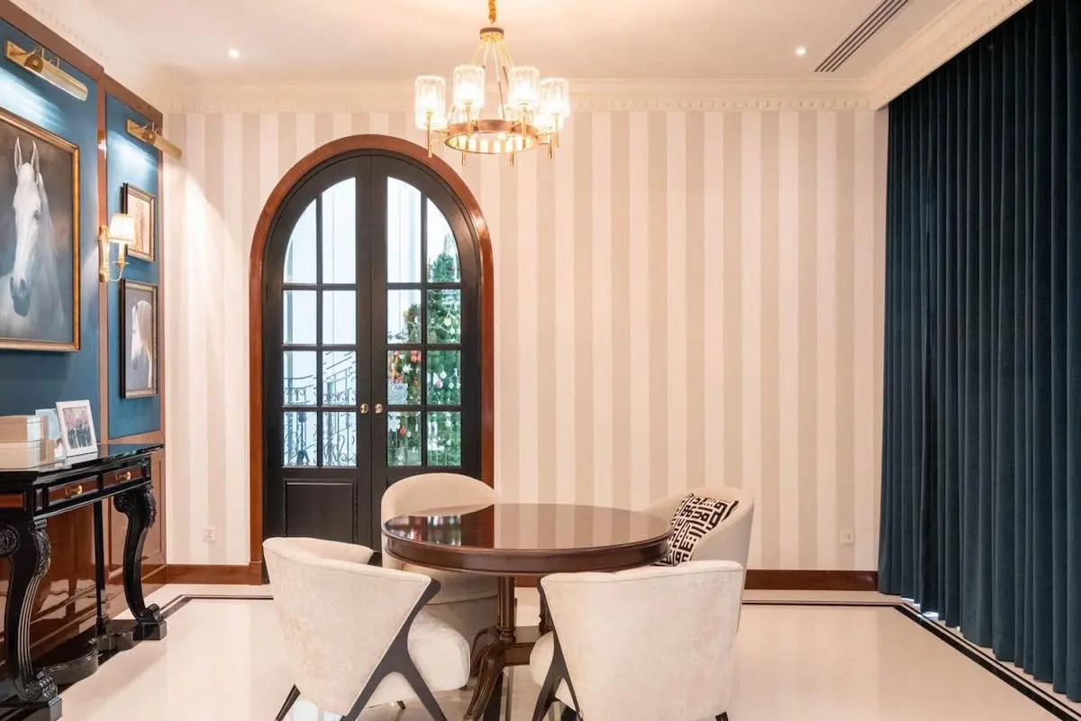 An elegant room with striped wallpaper, a chandelier, round table, chairs, and arched doors.