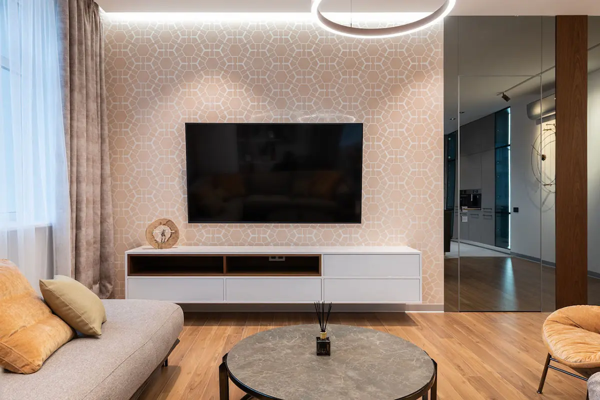 Modern living room with geometric wallpaper, a mounted TV, beige couch with pillows, and a round coffee table.