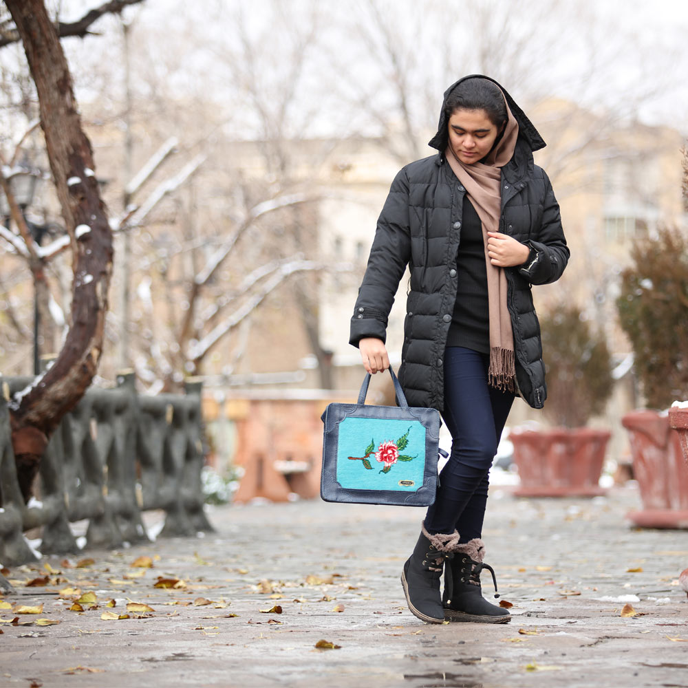 A girl standing with a blue leather bag in her hand.